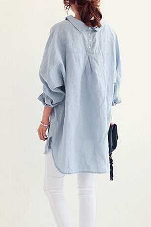Back view of woman wearing light blue oversized linen shirt with rolled sleeves and white pants
