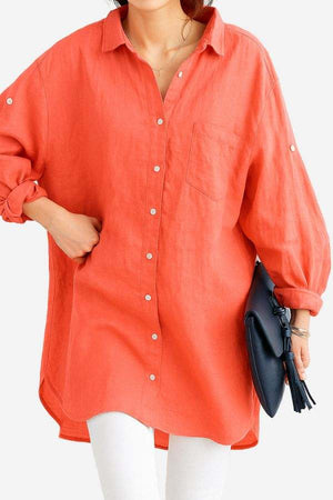 Woman wearing oversized coral linen shirt with rolled sleeves and front pocket, styled casually with white pants and navy clutch handbag