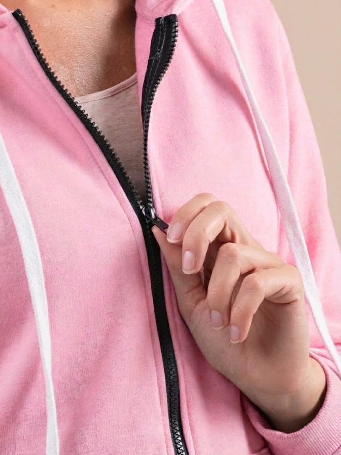 Close-up of a person wearing a pink oversized long zip sweatshirt hoodie with black zipper and white drawstrings.