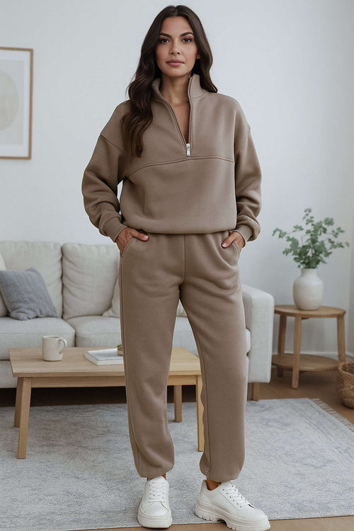 Woman wearing neutral toned cotton blend tracksuit with zip neckline and stretch waistband in a modern living room
