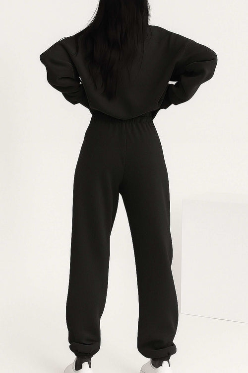 Back view of woman wearing black cotton blend tracksuit with stretch waistband and cuffs, showcasing relaxed fit and minimalist style.