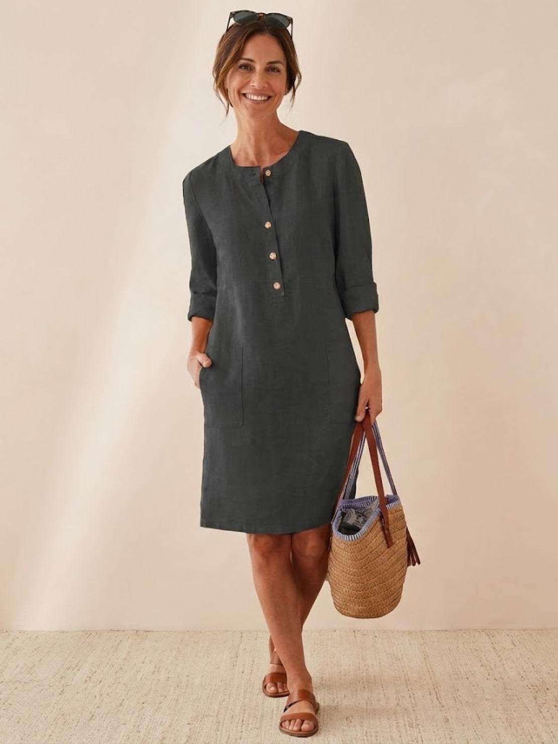 Woman wearing a knee-length dark cotton dress with rolled ¾ sleeves and button front, holding a woven bag.