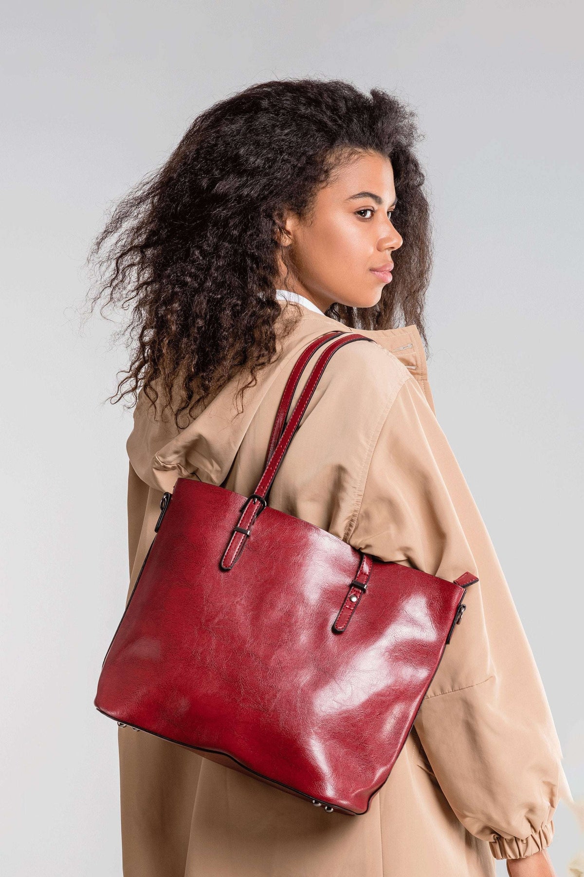 Woman wearing beige coat carrying red multi strap tote shopper bag over shoulder