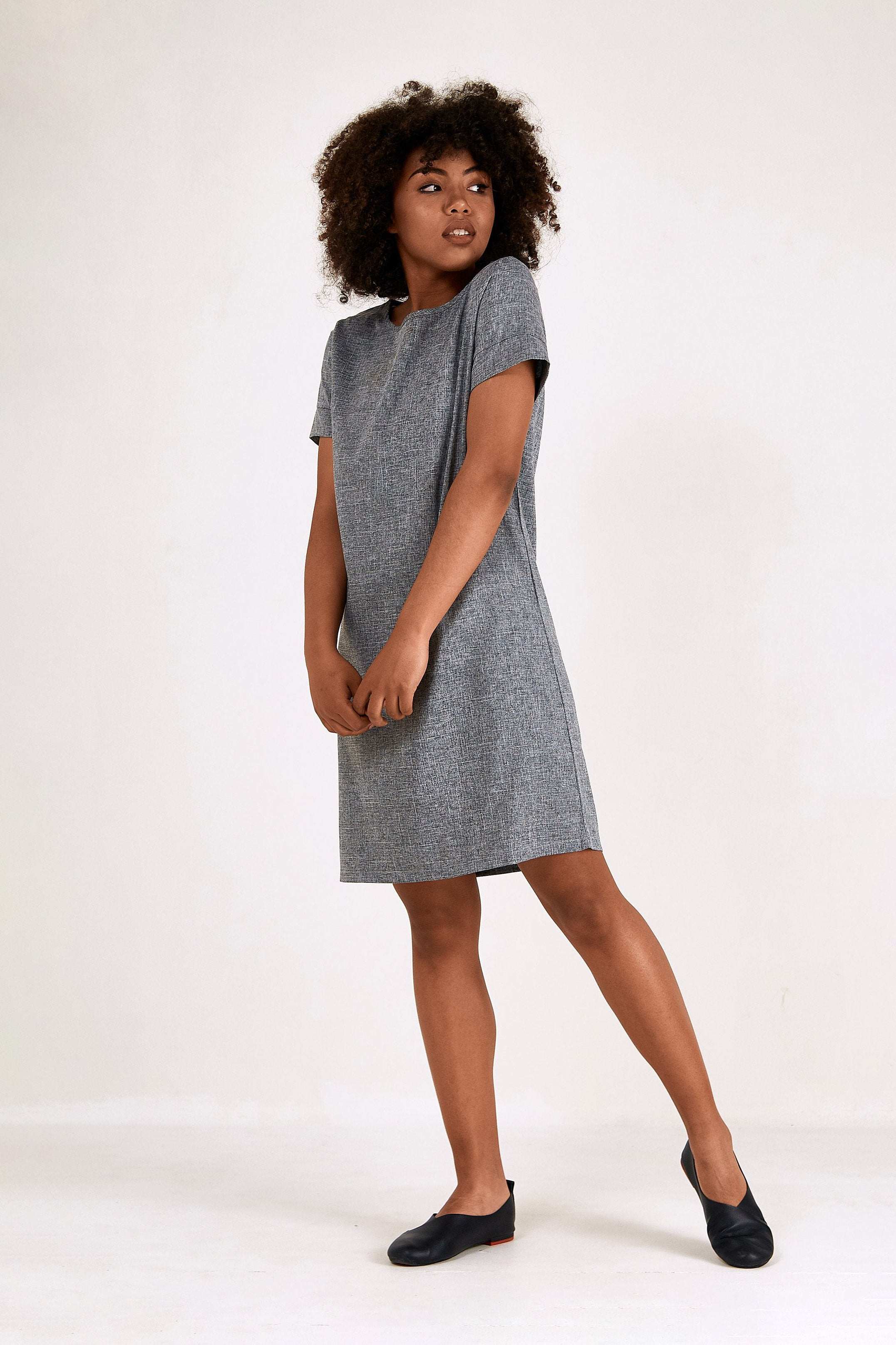 Woman wearing grey short sleeve shift dress with round neck and side pockets, knee-length professional style