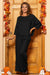 Woman wearing black 100% cotton linen monochrome two-piece set standing by wooden door decorated with autumn leaves and pumpkins holding a glass of wine.