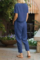 Back view of woman wearing blue breathable cotton linen set with relaxed fit short-sleeve top and straight-leg pants outdoors