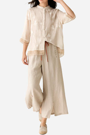 Woman wearing 100% cotton linen Tuscany two-piece set with sheer embroidered top and wide-leg trousers in beige tones.