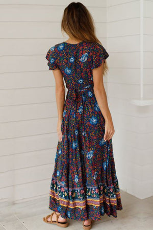 Woman wearing a Bohemian floral print wrap dress with ruffle sleeves and a waist tie, standing indoors viewed from the back.