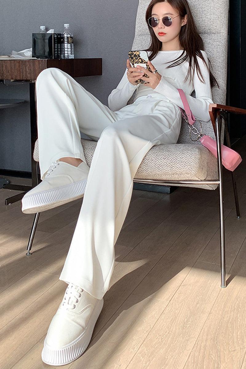 Woman wearing casual loose wide-leg high-waisted white pants with sneakers sitting on chair indoors