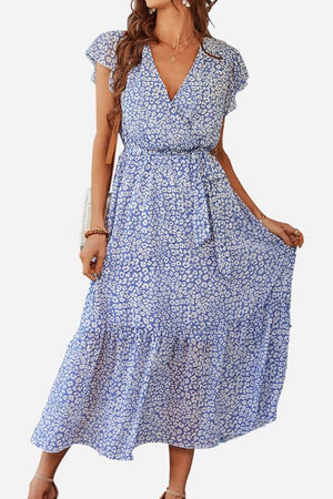 Woman wearing Elegant Blossoms Boho Maxi Dress with floral pattern, V-neck, short sleeves, and belted ruffle hem in soft blue tones.