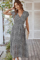 Woman wearing Elegant Blossoms Boho Maxi Dress with floral pattern and belted ruffle hem on porch background