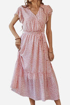 Woman wearing an Elegant Blossoms Boho Maxi Dress in soft pink floral wrap design with V-neck and belted ruffle hem