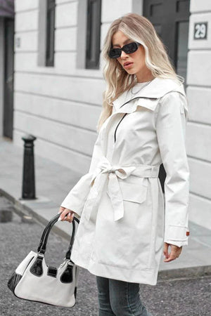 woman wearing white water-resistant windbreaker trench jacket with belt and sunglasses carrying handbag outdoors