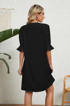 Back view of a woman wearing a black Dainty Charm Casual Ruffle Dress with ruffled sleeves, standing indoors.