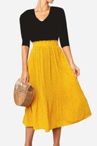 Woman wearing an effortlessly chic yellow polka dot pleated midi skirt with a high waist and black top carrying a wooden handbag.