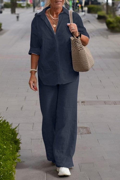 Woman wearing a relaxed shirt and trousers two-piece set in dark color walking outdoors with a handbag and white shoes.