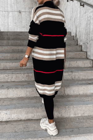 Cozy striped long knitted cardigan with oversized fit and soft fabric, black, beige, and red stripes, worn with black leggings and white sneakers.