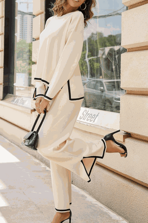 woman wearing long sleeved relaxed fit two-piece lounge set with black trim carrying black handbag and heels outdoors