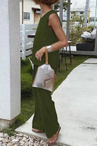 Woman wearing loose solid color sleeveless two-piece set in olive green outdoors with transparent handbag and sandals