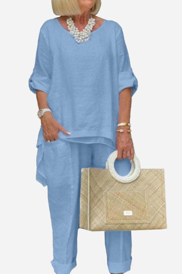 Woman wearing light blue asymmetrical two-piece trouser set with rolled-up sleeves and holding beige woven handbag