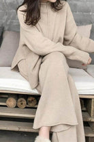 Woman wearing beige high neck sweater and wide leg pants lounge set sitting on a bench with neutral cushions