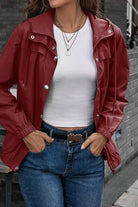 Woman wearing red outdoor hooded raincoat with snap buttons and elastic cuffs over white top and blue jeans