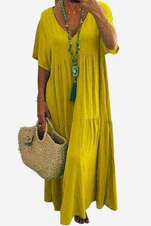 Yellow V-neck two-tiered maxi swing dress with loose sleeves and flowy silhouette worn with turquoise necklace and woven bag