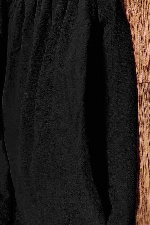 Black capped-sleeve voluminous pleated midi dress with airy sleeves and pockets on wood floor background