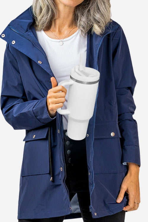 Person holding a white indestructible travel cup with handle, wearing a navy blue jacket and white shirt.