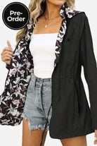 Woman wearing reversible floral raincoat with black exterior and floral print interior, paired with white top and denim shorts