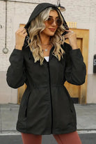 Woman wearing a black reversible floral raincoat with hood and zipper, styled for all-weather confidence and elegant fit