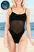 Black mesh tan-through one piece swimsuit with thin straps worn on beach background for even tanning without lines
