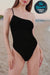 Woman wearing black asymmetric one-shoulder one-piece swimsuit with anti-tan line technology fabric on beach