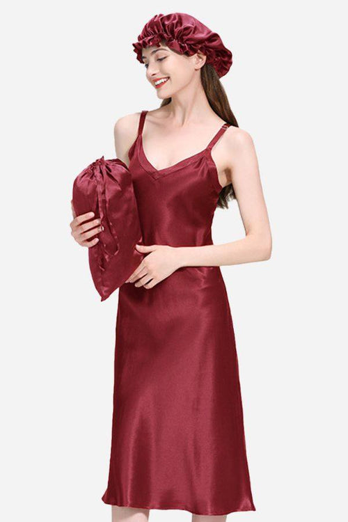 Woman wearing a burgundy 100% mulberry silk elegant night dress holding matching silk pillow and wearing silk bonnet