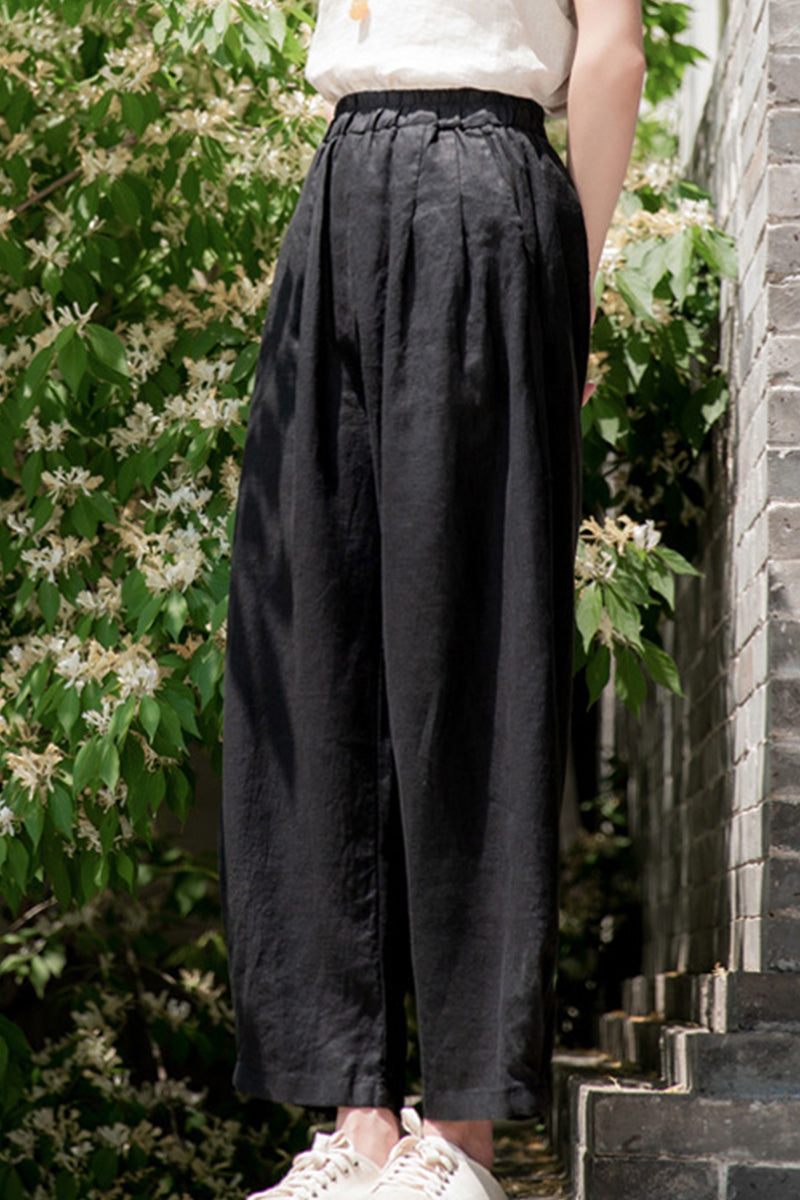 Black Ramie Linen Cotton Pants with relaxed fit and pleats, lightweight and breathable fabric blend, styled outdoors.
