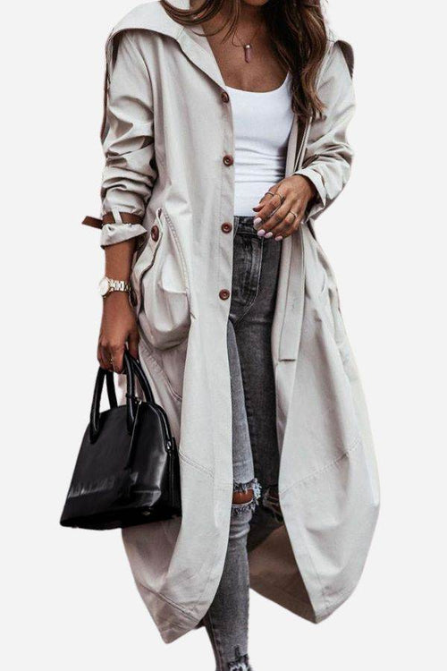 Woman wearing a beige oversized minimalist hooded coat with buttons, paired with a white tank top, ripped gray jeans, and holding a black handbag.