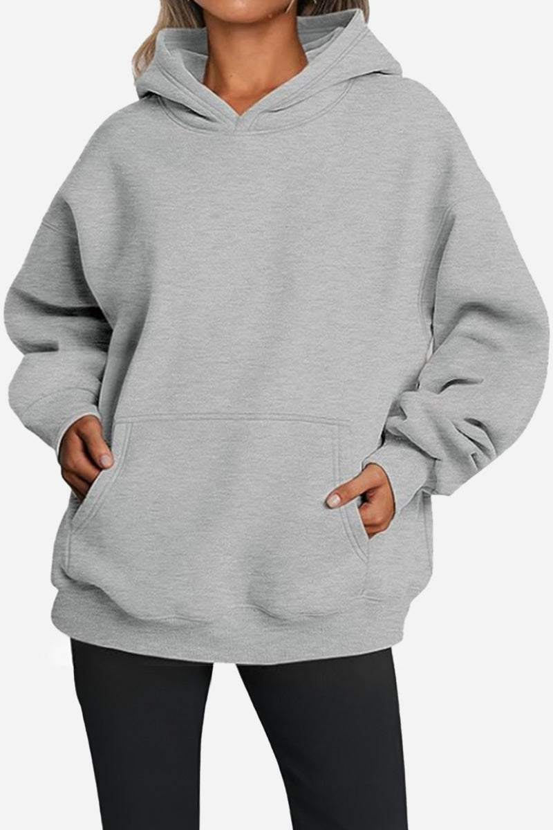 Woman wearing a grey oversized fleece-lined hoodie with a front pocket and relaxed fit.