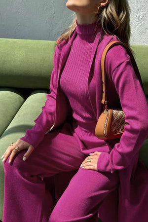 Woman wearing a one-size, magenta premium three-piece collection with a ribbed top, pants, and matching cardigan, styled with a brown shoulder bag.