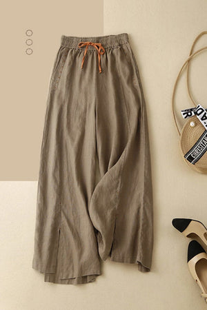 Brown wide-leg cotton linen Tuscany trousers with elastic waistband and drawstring on beige background with handbag and shoes.