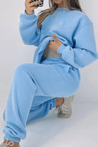 Woman wearing light blue Classic Comfort Athleisure set with sweatshirt and joggers sitting on the floor taking a mirror selfie