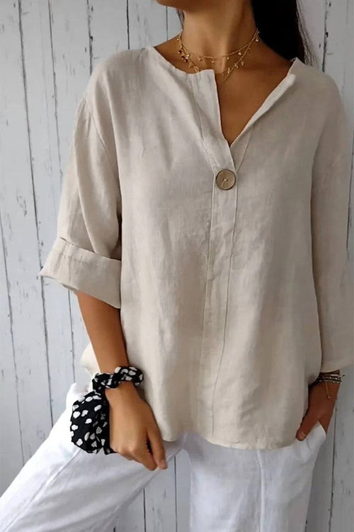 Woman wearing pure linen age-defying shirt with button detail and rolled sleeves, paired with white pants and black polka dot scrunchie.