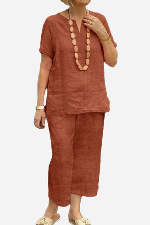 Woman wearing rust-colored breezy cotton blend two-piece set with short sleeves and loose pants, styled with wooden bead necklace and sandals.