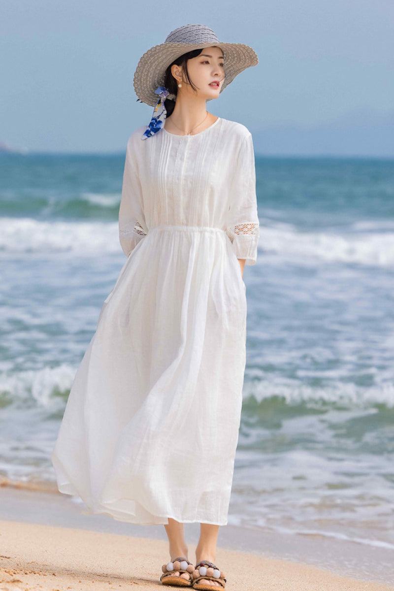 woman in white 100% linen coastal shift dress on beach with straw hat and sandals
