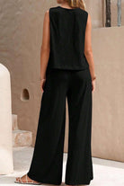 Woman wearing black sleeveless wide leg pants set standing against beige textured wall