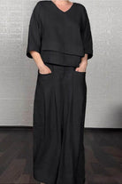Woman wearing black Atelier Serenity Layered Two-Piece Set with V-neck layered top and wide-leg trousers standing indoors