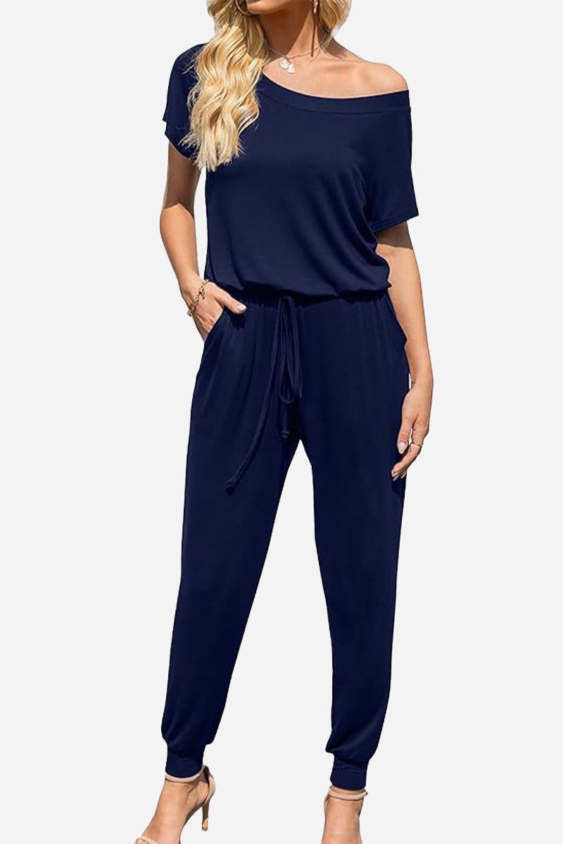 Woman wearing a navy blue Moonlit Rome Off-Shoulder jumpsuit with short sleeves and tapered legs, featuring a relaxed fit and drawstring waist.