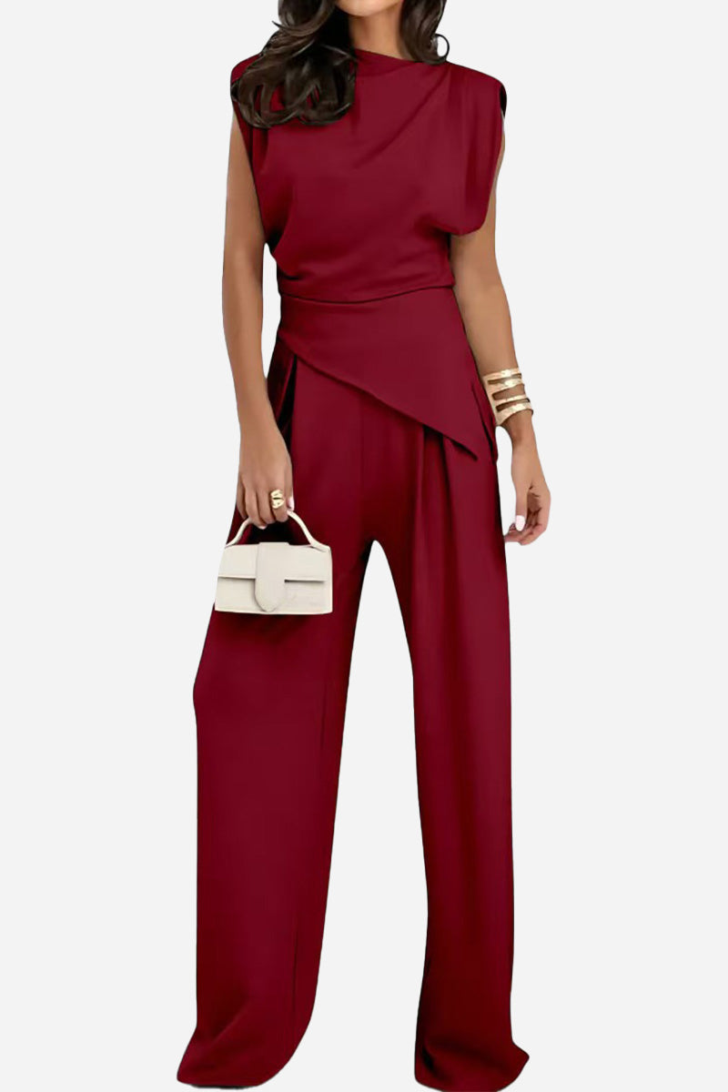 Woman wearing Manhattan Lines Draped sleeveless asymmetrical top and wide-leg pants in deep red holding a white handbag.