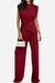 Woman wearing Manhattan Lines Draped sleeveless asymmetrical top and wide-leg pants in deep red holding a white handbag.