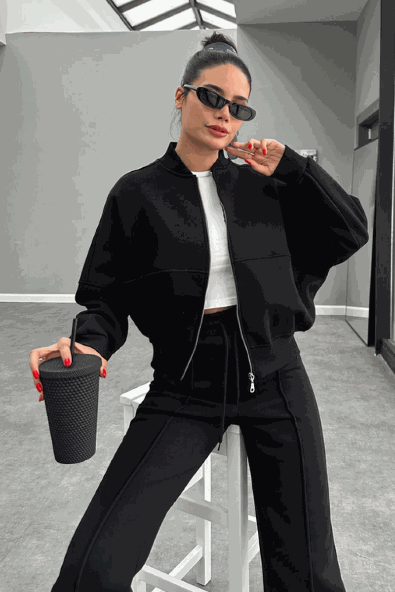 Woman wearing The Voyager Zip Set black zip-front sweatshirt and wide-leg joggers holding a drink cup, styled for travel and casual wear