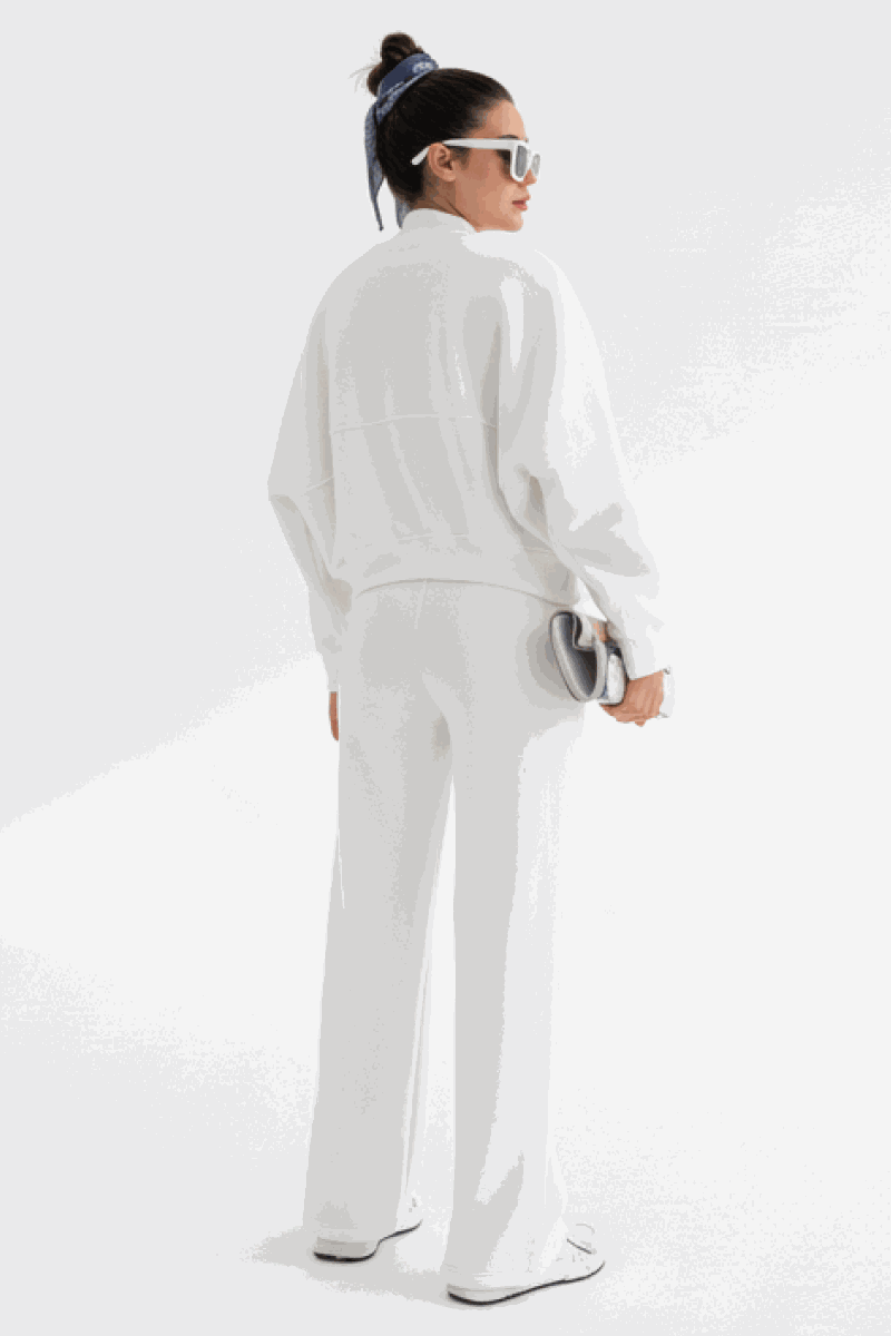 Woman wearing white Voyager Zip Set with zip-front sweatshirt and wide-leg joggers, styled with sunglasses and hair scarf, standing against white background